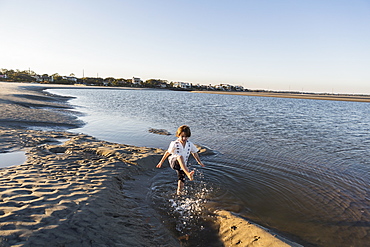 A six year old boy on the beach splashing in shallow water, St Simon's Island, Georgia, United States