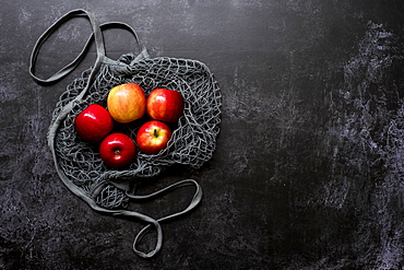 High angle close up of red apples in grey net bag on black background, United Kingdom