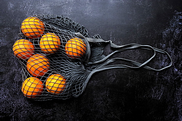 High angle close up of oranges in grey net bag on black background, United Kingdom