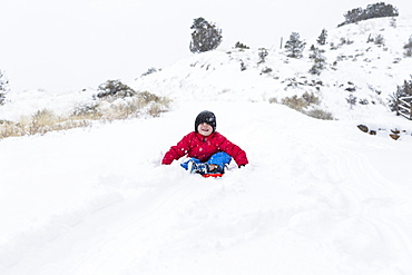 A boy and girl sledding down hill in snow, United States