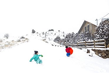 A boy and girl sledding down hill in snow, United States