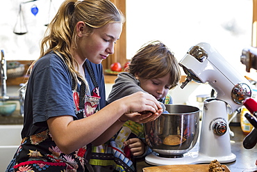 A teenage girl and her 6 year old brother in a kitchen, using a mixing bowl, United States