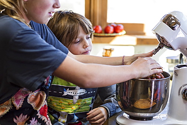 A teenage girl and her 6 year old brother in a kitchen, using a mixing bowl, United States