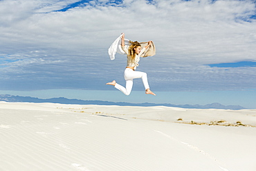 A teenage girl dancing and leaping n mid air in the open space on white sand dunes, White Sands National Monument, New Mexico, United States