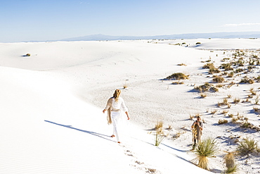 A teenage girl walking across sand dunes leaving footprints, White Sands National Monument, New Mexico, United States