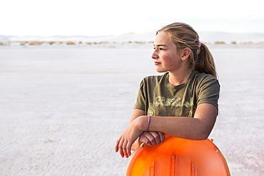 A teenage girl leaning on orange sled, White Sands National Monument, New Mexico, United States