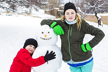 Brother and sister, a young boy and teenage girl leaning on snowman in winter