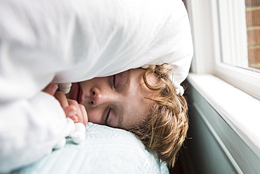 A six year old boy in bed with covers over his head