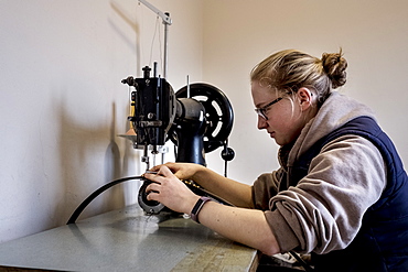 Female saddler sitting in workshop, sewing on saddlery sewing machine, Berkshire, United Kingdom