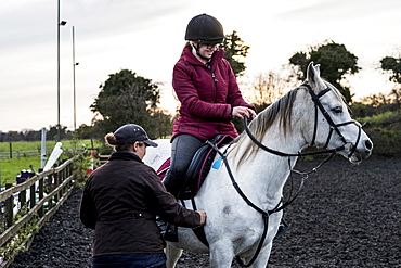 Young woman riding on white Cob horse in paddock, Berkshire, United Kingdom