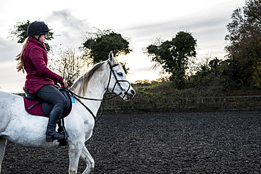 Young woman riding on white Cob horse in paddock, Berkshire, United Kingdom