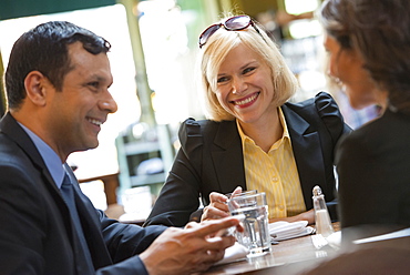 Business people outdoors, keeping in touch while on the go. Three people, a man and two women sitting at a table. A meeting or social gathering. 