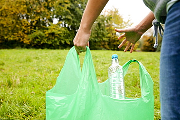 Woman stuffing soft waste plastics into large plastic bottle to make an ecobrick for use as a building block, Bristol, United Kingdom