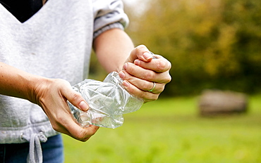 Woman stuffing soft waste plastics into large plastic bottle to make an ecobrick for use as a building block, Bristol, United Kingdom