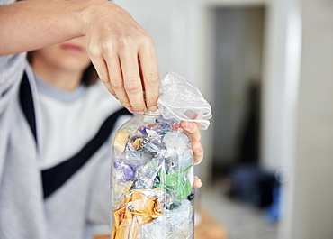 Woman stuffing soft waste plastics into large plastic bottle to make an ecobrick for use as a building block, Bristol, United Kingdom