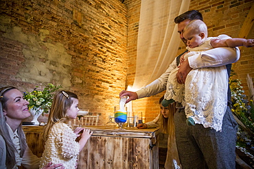 Family pouring coloured sand into glass jar during naming ceremony in an historic barn