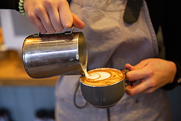 High angle close up of barista pouring milk foam onto cappuccino in a cup