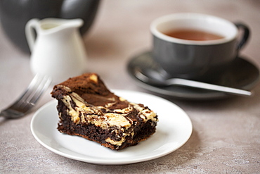 High angle close up of cup of tea and chocolate cheesecake on white plate in a cafe