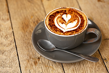 High angle close up of cup of cappuccino on rustic wooden table