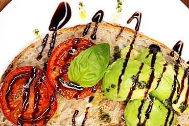 High angle close up of tomato and avocado bruschetta with balsamic vinegar reduction on a plate