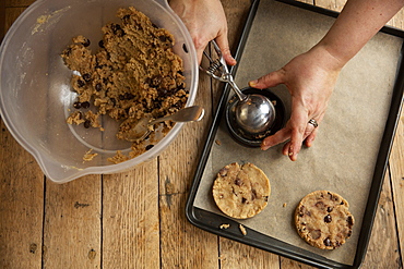 High angle close up of person standing at wooden table, baking chocolate chip cookies