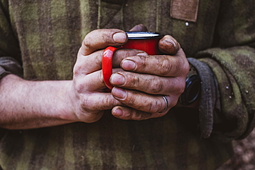 Close up of man with dirty hands holding red enamel mug, Devon, United Kingdom