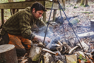 Man starting a camp fire in a forest, Devon, United Kingdom