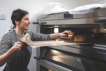 Artisan bakery making special sourdough bread, baker removing a tray of baked loaves from the oven