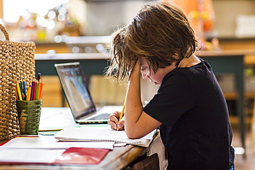 6 year old boy having a remote schooling session with his teacher, concentrating on writing