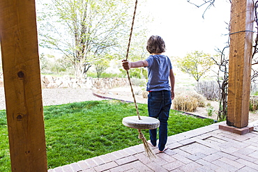 Six year old boy using a rope swing on a wide porch in the shade