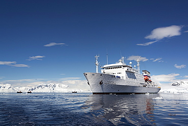 An Antarctic cruise ship with inflatable zodiacs on the calm waters among ice floes and mountainous landscape, Antarctic peninsula, Antarctica