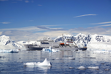 An Antarctic cruise ship with inflatable zodiacs on the calm waters among ice floes and mountainous landscape, Antarctic peninsula, Antarctica