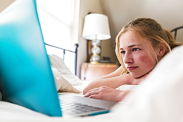 Teenage girl looking at laptop in bed