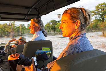 Senior woman and mature daughter, two generations of women in a safari jeep looking out at sunset, Moremi Game Reserve, Botswana