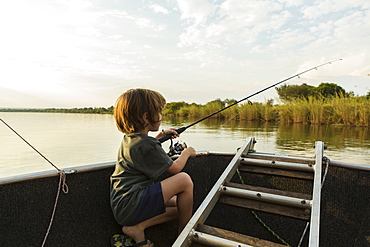 A five year old boy fishing from a boat on the Zambezi River, Botswana, Zambezi River, Botswana