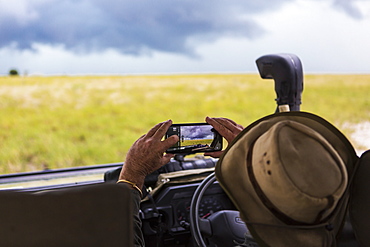 A safari guide taking smart phone picture of approaching storm clouds