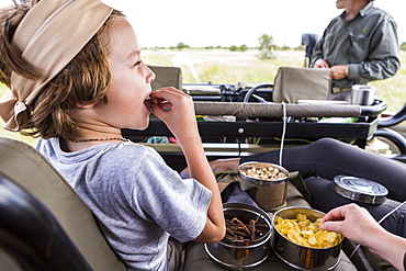 Six year old boy eating snacks in safari vehicle, Botswana