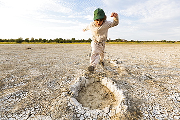 Six year old boy leaping into elephant footprints, Nxai Pan, Botswana