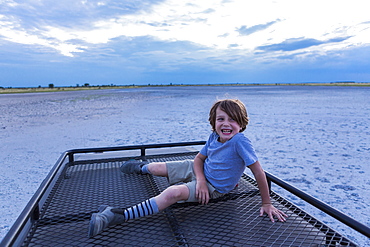 Six year old boy and guide on top of safari vehicle, Nxai Pan, Botswana