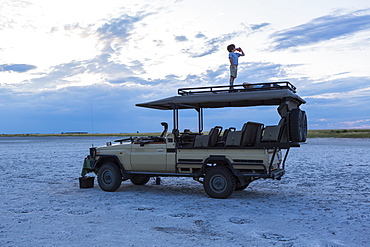 Six year old boy and older sister standing on top of safari vehicle, Nxai Pan, Botswana