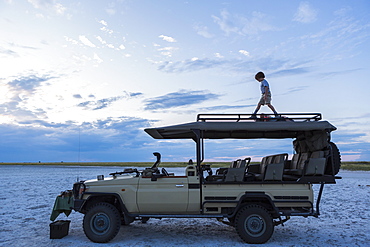 Six year old boy and older sister standing on top of safari vehicle, Nxai Pan, Botswana