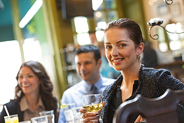 Business people outdoors, keeping in touch while on the go. Three people around a cafe table, one woman turning around, holding a wine glass.