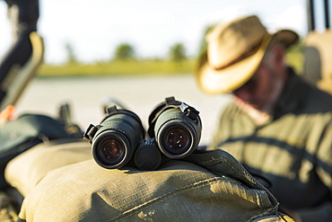 Binoculars on the dash of a safari jeep, a safari guide in the background