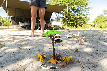 A safari scene on the sand, toy jeeps and safari animals on the ground, and an onlooker's legs