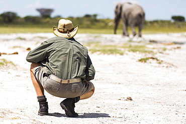 A guide crouching close to an elephant in Nxai Pan, Botswana