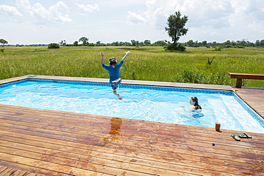 Six year old boy jumping into pool, tented camp, Botswana