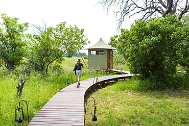 Thirteen year old girl walking wooden path, tented camp, Botswana