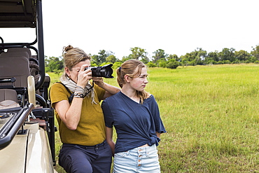 mother photographing with teen daughter near safari vehicle, Botswana