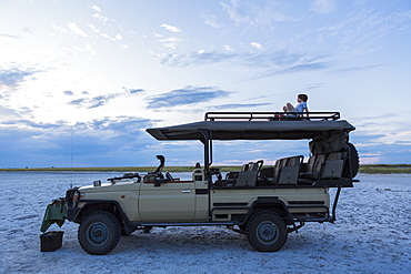 A six year old boy and his teenage sister sitting on top of a safari vehicle at dusk, Makgadikgadi Pan National Park, Botswana