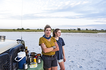 Mother and daughter on safari standing by a jeep at sunset, Makgadikgadi Pan National Park, Botswana